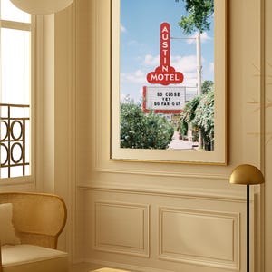 May include: Framed print featuring a vintage motel sign in Austin, Texas. The red sign reads "AUSTIN MOTEL" and "SO CLOSE YET SO FAR OUT" against a blue sky. The print is displayed in a room with a neutral color palette.