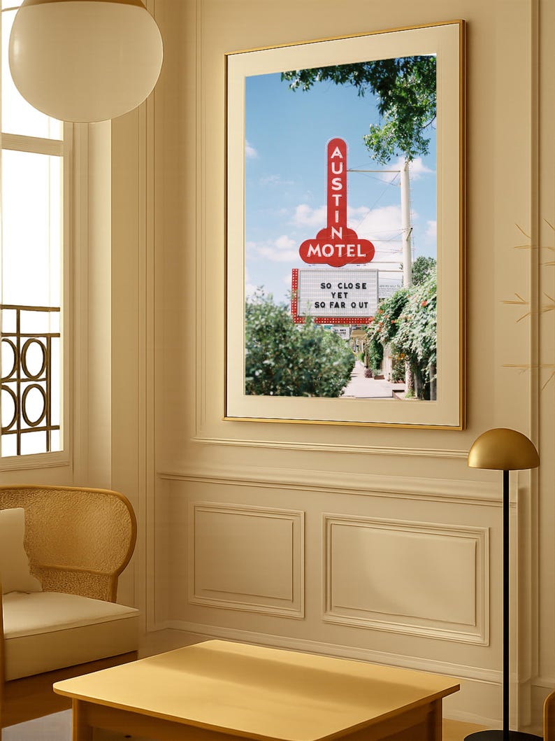 May include: Framed print featuring a vintage motel sign in Austin, Texas. The red sign reads "AUSTIN MOTEL" and "SO CLOSE YET SO FAR OUT" against a blue sky. The print is displayed in a room with a neutral color palette.