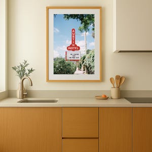 May include: A framed print featuring a vintage motel sign with the text "AUSTIN MOTEL" in red neon against a blue sky. The sign also displays the phrase "SO CLOSE YET SO FAR OUT". The print is displayed in a kitchen setting.