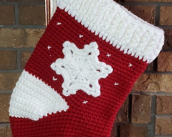 May include: A red and white crocheted Christmas stocking with a snowflake design. The stocking is hanging from a hook on a brick fireplace.