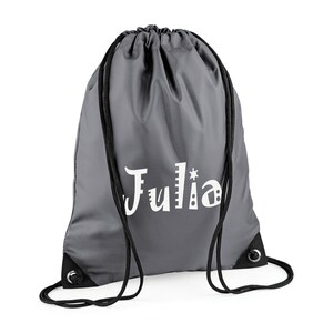 May include: A gray drawstring backpack with black drawstrings and grommets. The name "Julia" is printed in white, stylized lettering on the front of the bag. The bag is made of a smooth, possibly nylon, material.