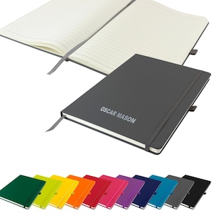 Puede incluir: Un cuaderno de tapa dura gris con cierre elástico negro y un marcapáginas de cinta gris. El cuaderno tiene el texto "OSCAR MASON" impreso en la portada. El cuaderno está abierto para revelar páginas rayadas. El cuaderno está disponible en una variedad de colores, incluyendo verde, amarillo, naranja, rojo, rosa, morado, azul, azul verdoso, gris y negro.