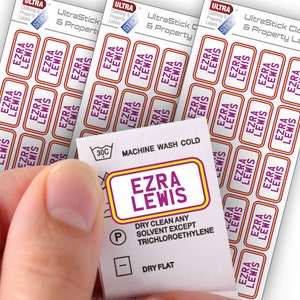 May include: A white clothing label with purple and yellow text that reads "UltraStick Clothing & Property Labels" and "Ezra Lewis". The label also includes care instructions for machine washing cold, dry cleaning, and dry flat.