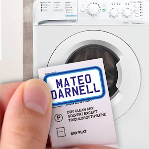 May include: A white care label with blue text that reads "Mateo Darnell" and instructions for dry cleaning. The label is held in a hand in front of a white washing machine.