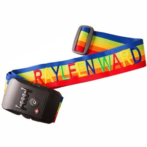 May include: A rainbow luggage strap with a combination lock. The strap is red, orange, yellow, green, blue, and purple. The lock is black and has a red button. The strap is personalized with the name "RAYLEEN WARD".