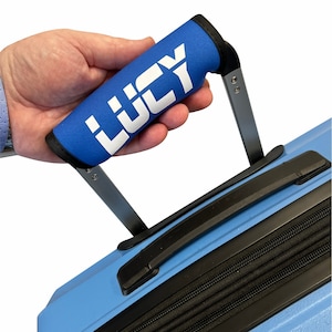 Puede incluir: Asa de maleta azul con una funda para asa de maleta personalizada azul y blanca que dice "LUCY" en letras blancas.