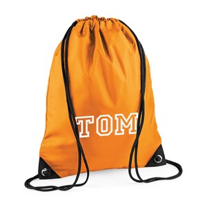 May include: Orange drawstring bag with the name "TOM" printed in white block letters. The bag has black drawstrings and black reinforced corners. The bag is made of a smooth, possibly nylon, material.