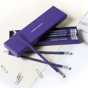 May include: A purple pencil box with a set of purple pencils with the name "Elizabeth Marlow" printed on them.