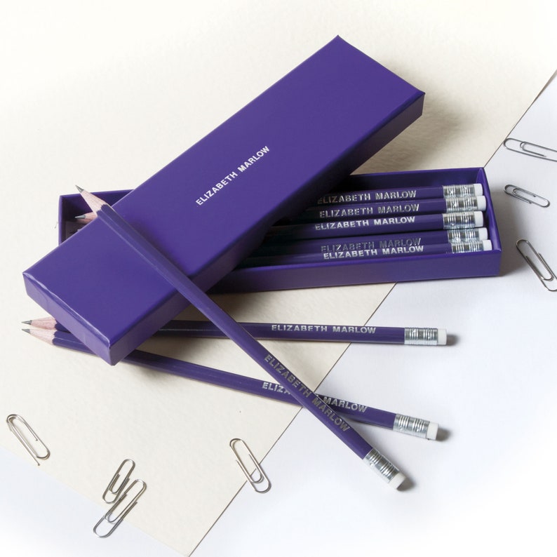 May include: A purple pencil box with a set of purple pencils with the name "Elizabeth Marlow" printed on them.