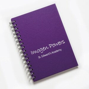 Op de afbeelding: Paarse spiraalgebonden notitieboek met de tekst "Imogen Powers" en "St. Edward's Academy" in witte letters.