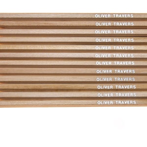 May include: A set of twelve wooden pencils with white lettering that reads "OLIVER TRAVERS" on each pencil. The pencils are arranged vertically with the coloured ends facing the viewer.