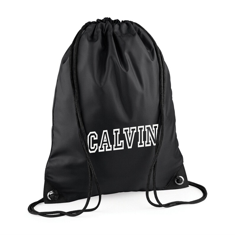 May include: Black drawstring backpack with the name "CALVIN" printed in white block letters. The bag has black drawstrings and metal eyelets. The bag is made of a smooth, possibly nylon, material.