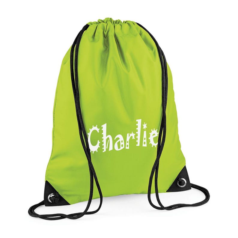 May include: A lime green drawstring backpack with black drawstrings and corner reinforcements. The name "Charlie" is printed in white, stylized lettering across the front of the bag. The bag is made of a lightweight, possibly nylon, material.