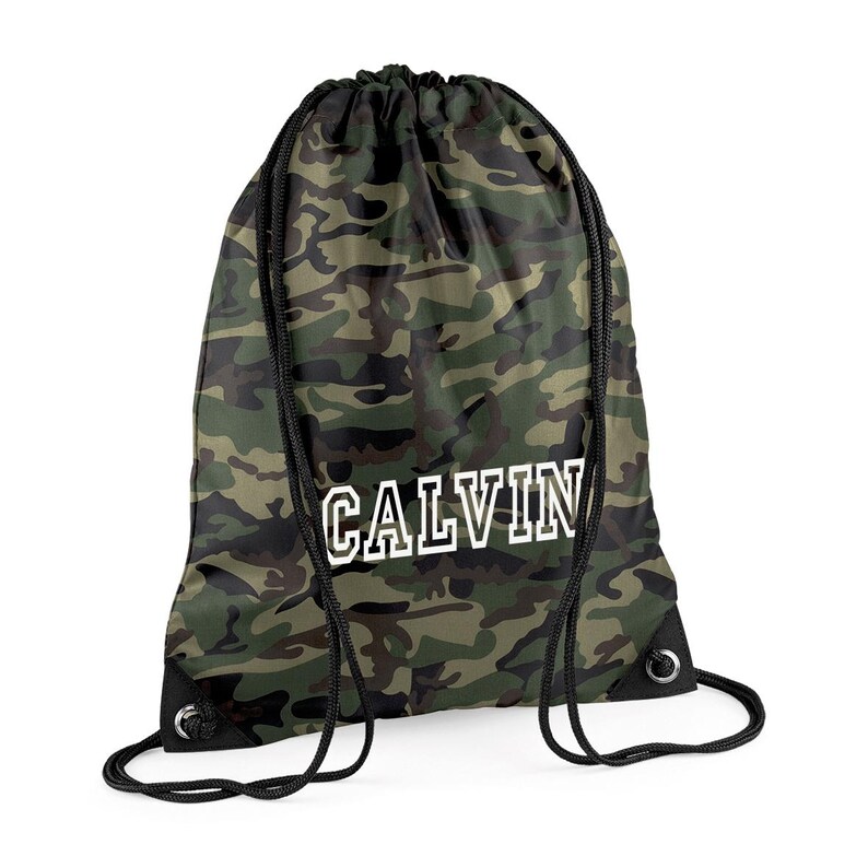 May include: A drawstring backpack with a camouflage pattern in shades of green, brown, and black. The word "CALVIN" is printed in white block letters across the front. The bag has black drawstrings and metal eyelets.