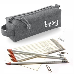 May include: A gray pencil case with the name "Lexy" in white script. The case has a zipper closure and a small handle. Several white pencils with "Lexi Logan" printed on them are arranged near the case, along with paperclips.