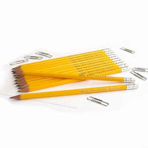 Puede incluir: Una pila de lápices amarillos con el texto "MRS WHITTAKERS PENCIL" impreso en cada lápiz. Los lápices están sobre una superficie blanca con clips de papel plateados esparcidos alrededor.