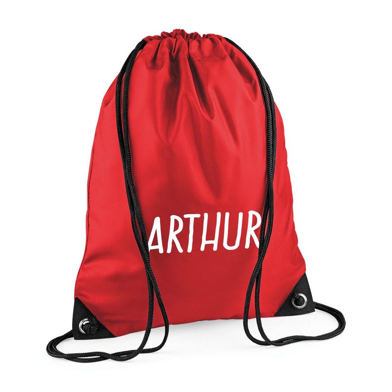 May include: A red drawstring backpack with the name "ARTHUR" printed in white. The bag has black drawstrings and reinforced black corners. This bag is suitable for carrying books, gym clothes, or other personal items.