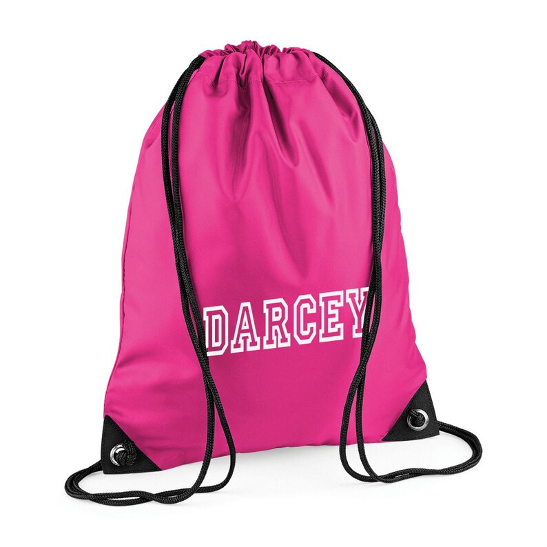 May include: A bright pink drawstring backpack with black drawstrings and grommets. The name "DARCEY" is printed in white, block letters across the front of the bag. The bag is made of a smooth, possibly nylon, material.