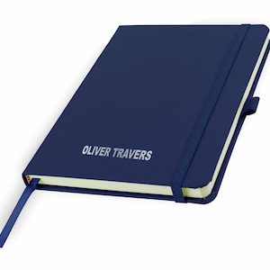 May include: A navy blue notebook with a matching elastic closure and a bookmark ribbon. The notebook has a cream-colored page edge and the name "OLIVER TRAVERS" is embossed in silver on the front cover.