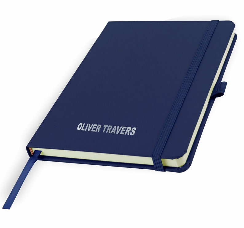 May include: A navy blue notebook with a matching elastic closure and a bookmark ribbon. The notebook has a cream-colored page edge and the name "OLIVER TRAVERS" is embossed in silver on the front cover.
