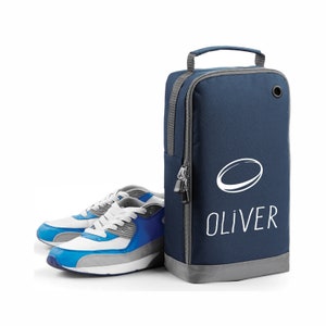 Puede incluir: Una bolsa de zapatos azul con un óvalo blanco y el nombre "OLIVER" impreso en ella. Dos zapatillas azules y blancas están delante de la bolsa.