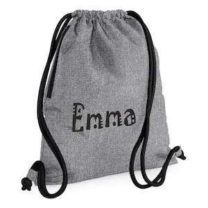 May include: A gray drawstring backpack with black drawstrings. The name "Emma" is printed in black, stylized letters on the front of the bag. The bag is made of a textured fabric.