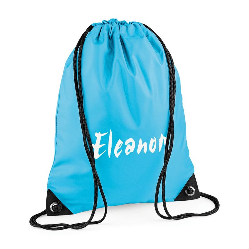 May include: A light blue drawstring backpack with black drawstrings and corner reinforcements. The name "Eleanor" is printed in white script across the front of the bag. The bag is made of a smooth, durable material.