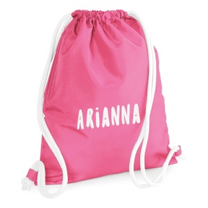 May include: A bright pink drawstring backpack with the name "ARIANNA" printed in white. The bag has white drawstrings and a white zipper. The bag is made of a smooth, possibly nylon, material.
