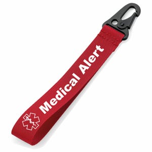Könnte beinhalten: Ein rotes Medical Alert-Band mit weißem Text "Medical Alert" und einem weißen medizinischen Symbol. Es hat einen schwarzen Metallclip zum Befestigen.