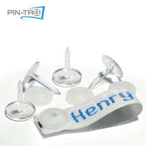 May include: Clear plastic push pins with a white fabric tag that reads "Henry" in blue. The pins have a flat, round head and a sharp point. The logo "PIN-TAG" is in the top left corner.