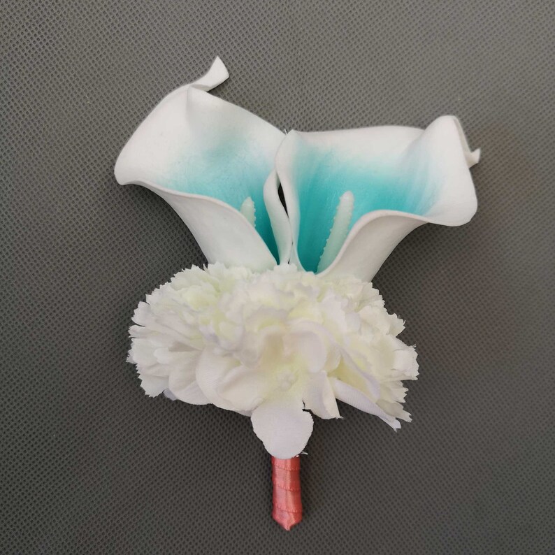 May include: A white and teal artificial flower boutonniere with a white carnation base and a pink stem.