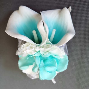 May include: A bouquet of white and turquoise artificial flowers. The bouquet features two calla lilies and several smaller flowers.