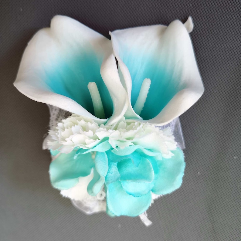 May include: A bouquet of white and turquoise artificial flowers. The bouquet features two calla lilies and several smaller flowers.