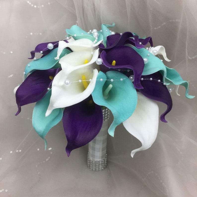 May include: A bridal bouquet of white, teal, and purple calla lilies with pearl accents.