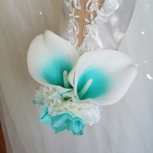 Puede incluir: Un ramo de novia con lirios blancos con detalles en turquesa, claveles blancos y una rosa turquesa.