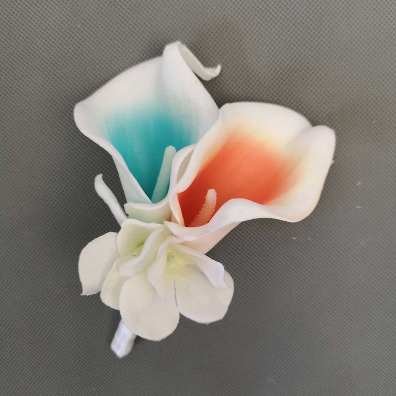 May include: A bouquet of three artificial calla lilies in white, teal, and peach colors. The flowers are arranged in a cluster with a small white flower at the base.