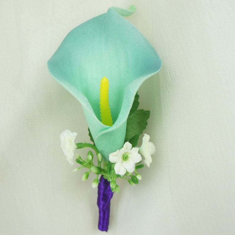 May include: A light blue artificial calla lily boutonniere with white baby's breath and a purple ribbon.