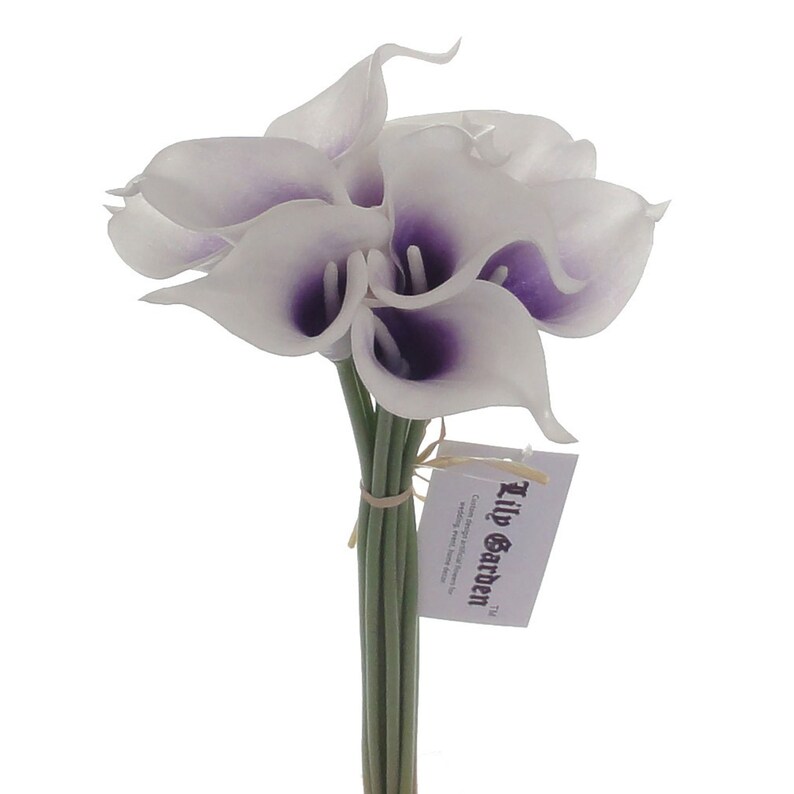 May include: A bouquet of white artificial calla lilies with purple centres. The stems are tied together with twine and a small tag that reads "The Lily Garden".