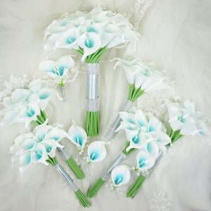 May include: A set of six white calla lily bouquets with blue accents. The bouquets are tied with silver ribbon and rhinestones. The bouquets are arranged on a white fabric background.