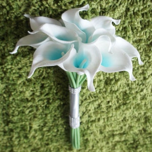 May include: A bouquet of white calla lilies with blue centers. The stems are wrapped in a silver ribbon with rhinestones.