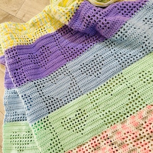 May include: A multi-colored crocheted blanket with stripes of yellow, purple, blue, green, pink, and brown. The blanket is made with a lacy stitch pattern.