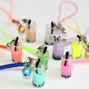 Op de afbeelding: Miniatuur kleurrijke bubble tea bedels met zwarte rietjes. Elke bedel heeft een andere kleur, waaronder roze, groen, blauw en geel, met een kleine bel en een koord in bijpassende kleuren. De bedels staan op een witte achtergrond.