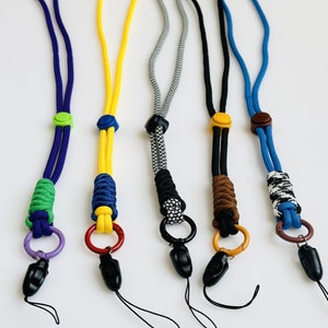 Può includere: Cinque lacci per telefono colorati con diversi motivi e colori. Ogni laccio ha un anello di metallo e un fermaglio di plastica all'estremità.