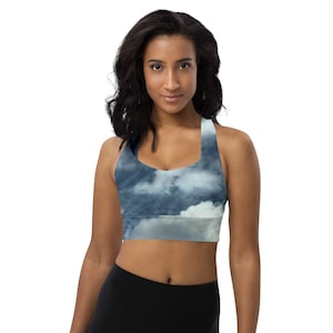 Puede incluir: Una mujer lleva un sujetador deportivo azul y blanco con un estampado de nubes. El sujetador tiene un estilo de espalda de nadador y está hecho de una tela elástica y cómoda.