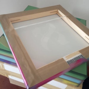 May include: A wooden frame with a white canvas stretched over it. The frame is wrapped in a rainbow-colored tape. The frame is sitting on top of a stack of boxes.