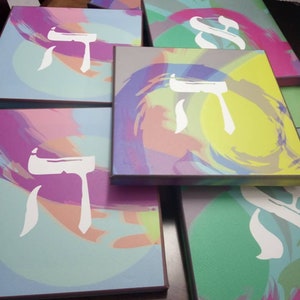 May include: A stack of colorful canvases with a white Hebrew letter painted on each. The canvases have a variety of abstract designs in shades of pink, purple, blue, green, and yellow.