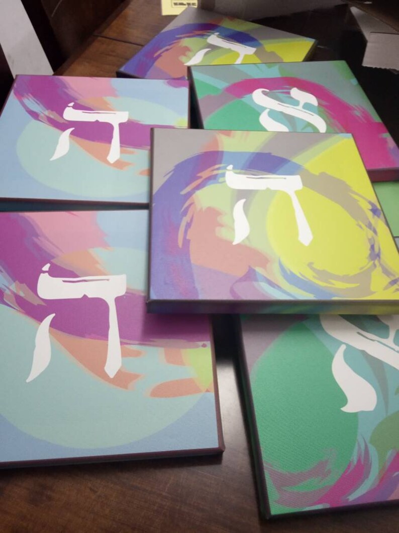 May include: A stack of colorful canvases with a white Hebrew letter painted on each. The canvases have a variety of abstract designs in shades of pink, purple, blue, green, and yellow.