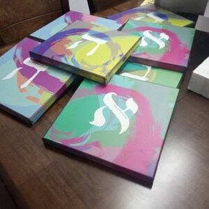 May include: A stack of colorful canvases with abstract designs and the letter 'T' in white on each canvas.