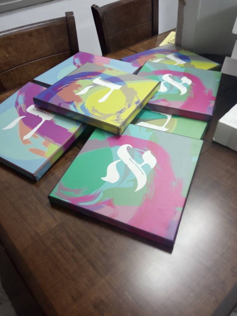 May include: A stack of colorful canvases with abstract designs and the letter 'T' in white on each canvas.