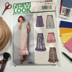 May include: A sewing pattern from New Look features skirt designs. The pattern includes a photo of a woman wearing a pink floral skirt. The pattern's text includes "easy" and "size A 8-18". Other sewing supplies are in the background.